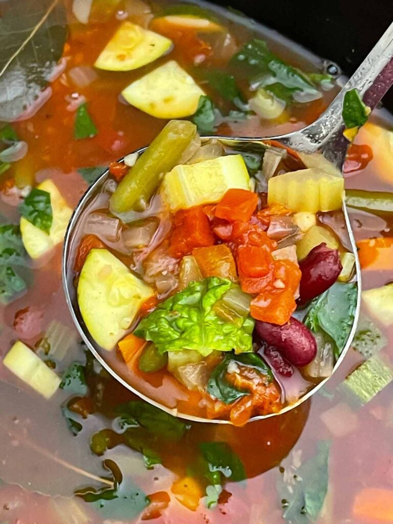Finished minestrone soup with tender vegetables, beans, spinach, and tomato broth in the slow cooker.