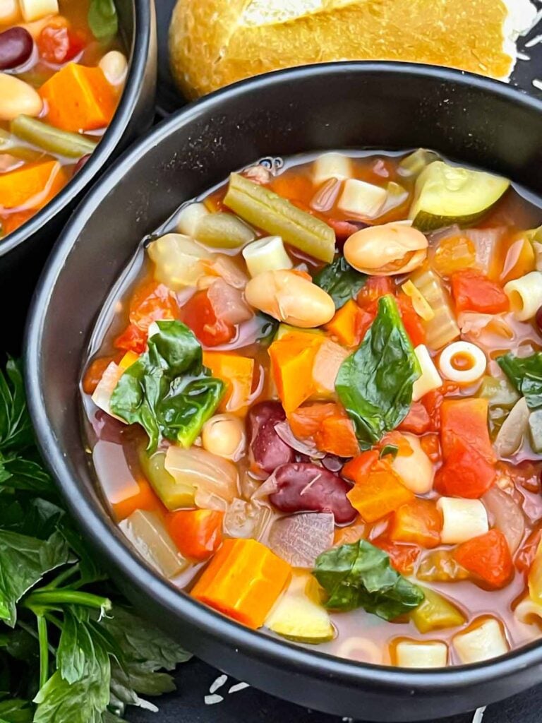 Finished minestrone soup with tender vegetables, beans, spinach, and tomato broth.
