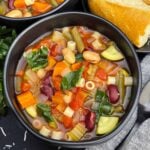 Bowls of slow cooker minestrone soup with Ditalini pasta, vegetables, beans, and spinach.