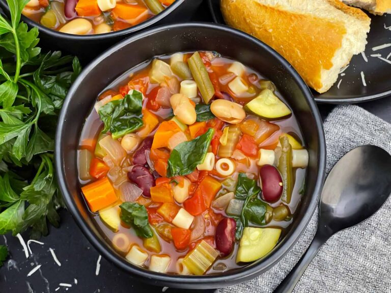 Bowls of slow cooker minestrone soup with Ditalini pasta, vegetables, beans, and spinach.