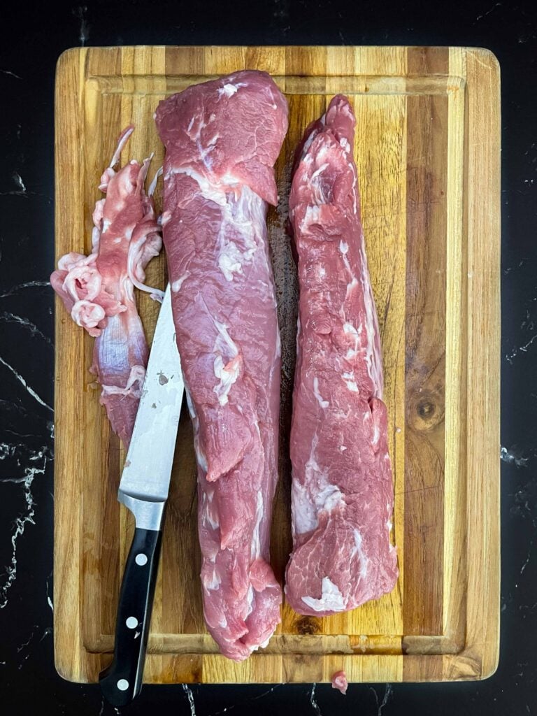 Two pork tenderloins trimmed of silver skin on a wooden cutting board.
