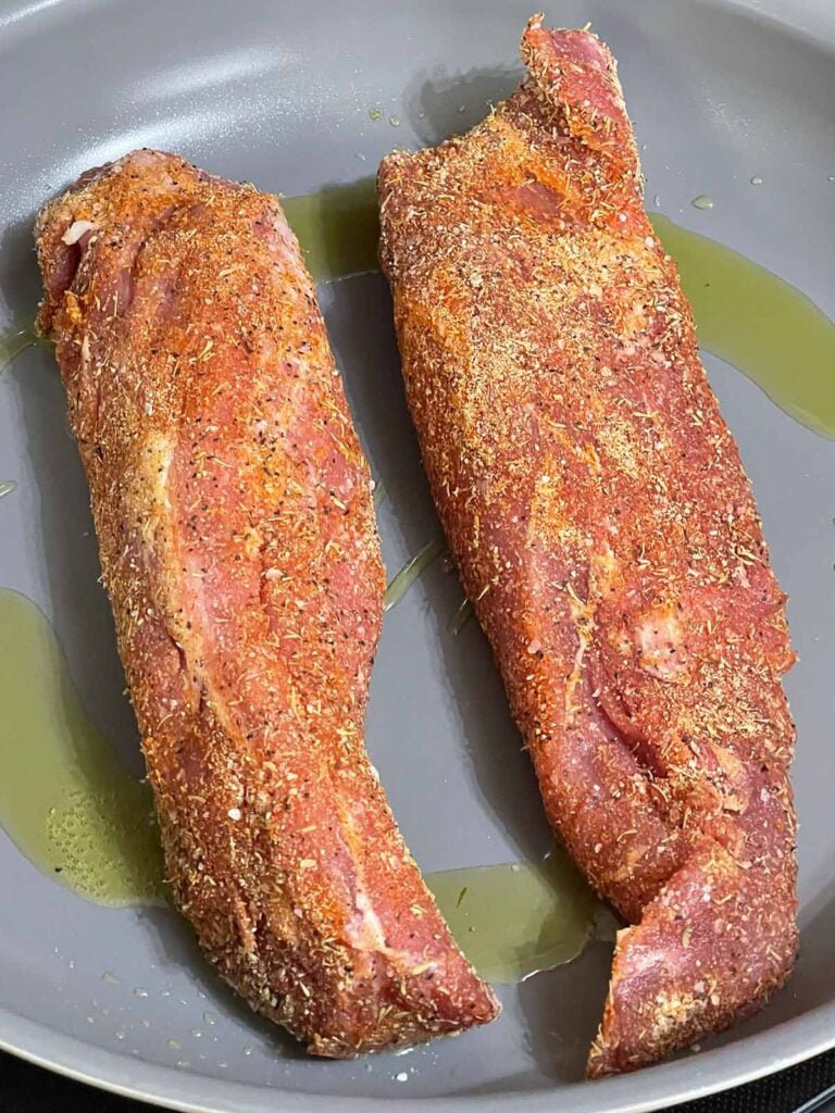 Seasoned pork tenderloins searing in a hot skillet.