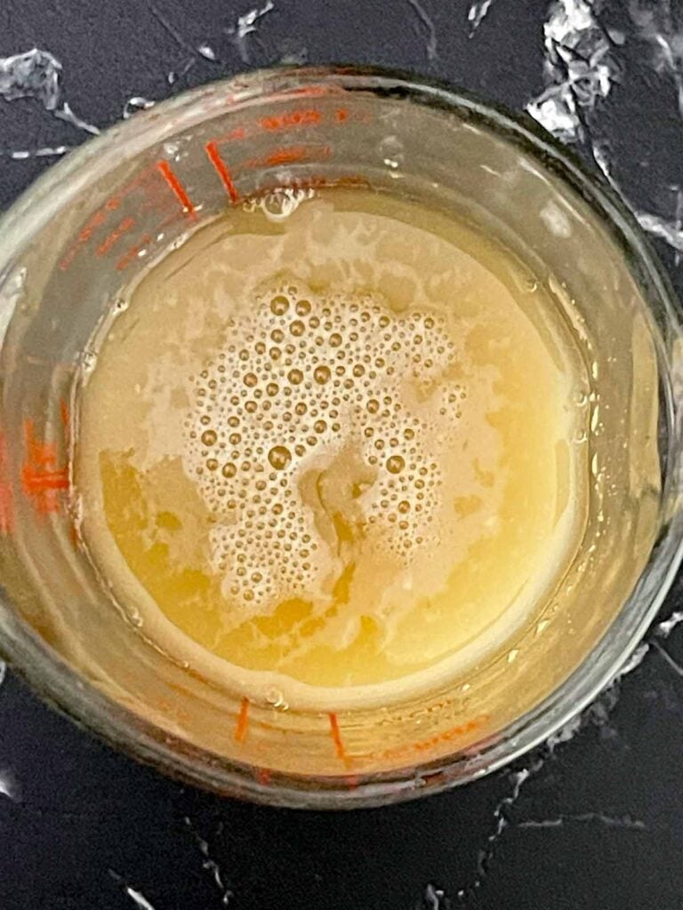 Active dry yeast added to warm water and honey in a measuring cup.
