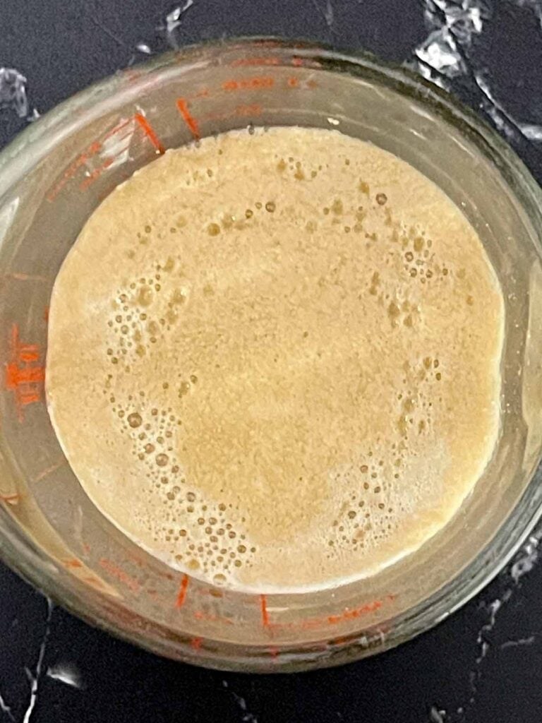 Bloomed yeast mixture foamy on top in a measuring cup.