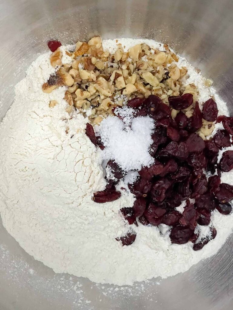 Flour, dried cranberries, chopped walnuts, and salt added to a stand mixer bowl.