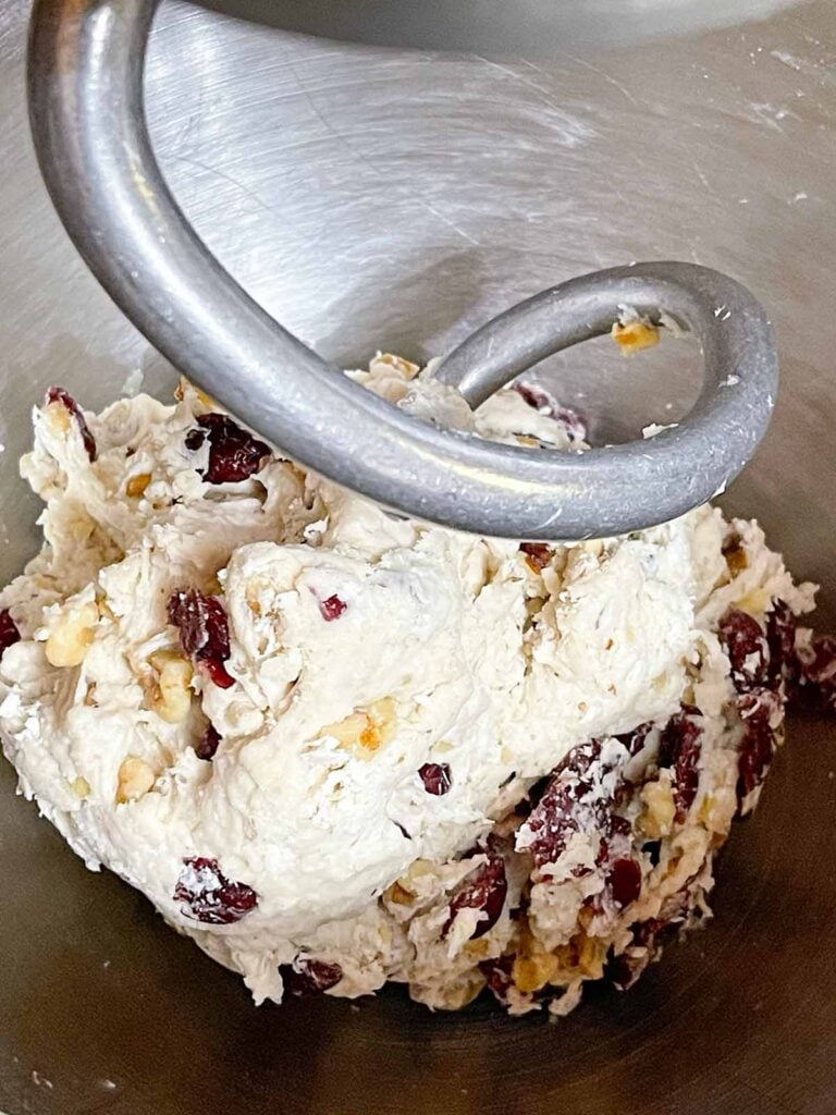Cranberry walnut bread dough kneading with a dough hook in a stand mixer.