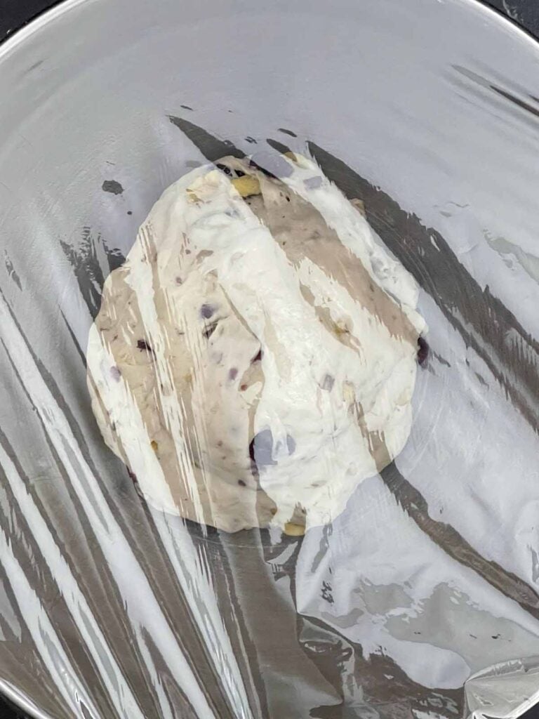 Cranberry walnut bread dough shaped into a ball and covered with plastic wrap for the first rise.