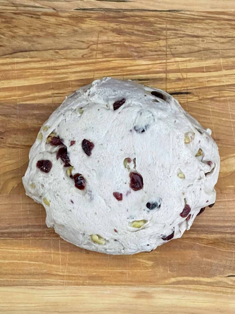 Risen cranberry walnut bread dough turned out onto a wooden board.