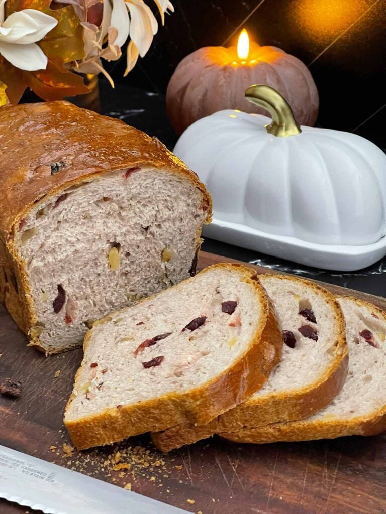 Sliced cranberry walnut bread on a cutting board showing the cranberries and walnuts throughout the loaf.