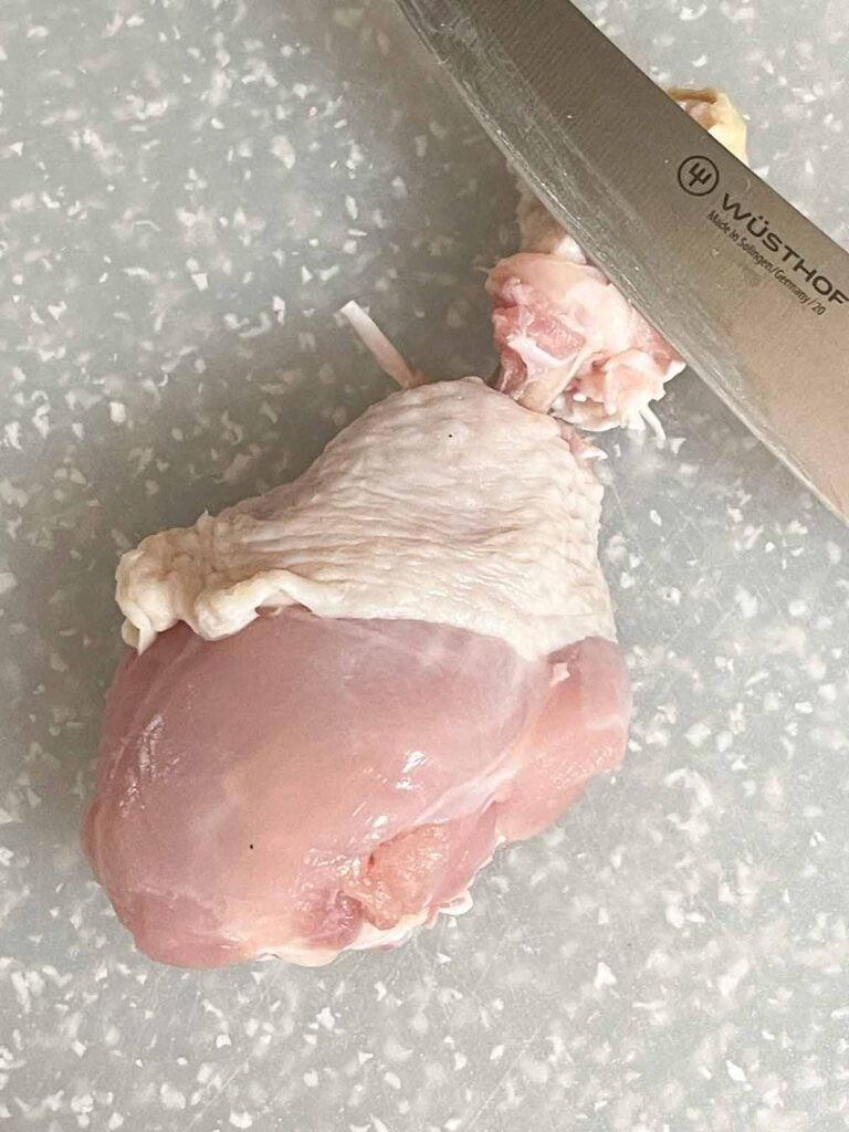 Chicken skin cut completely around the drumstick to expose the bone.