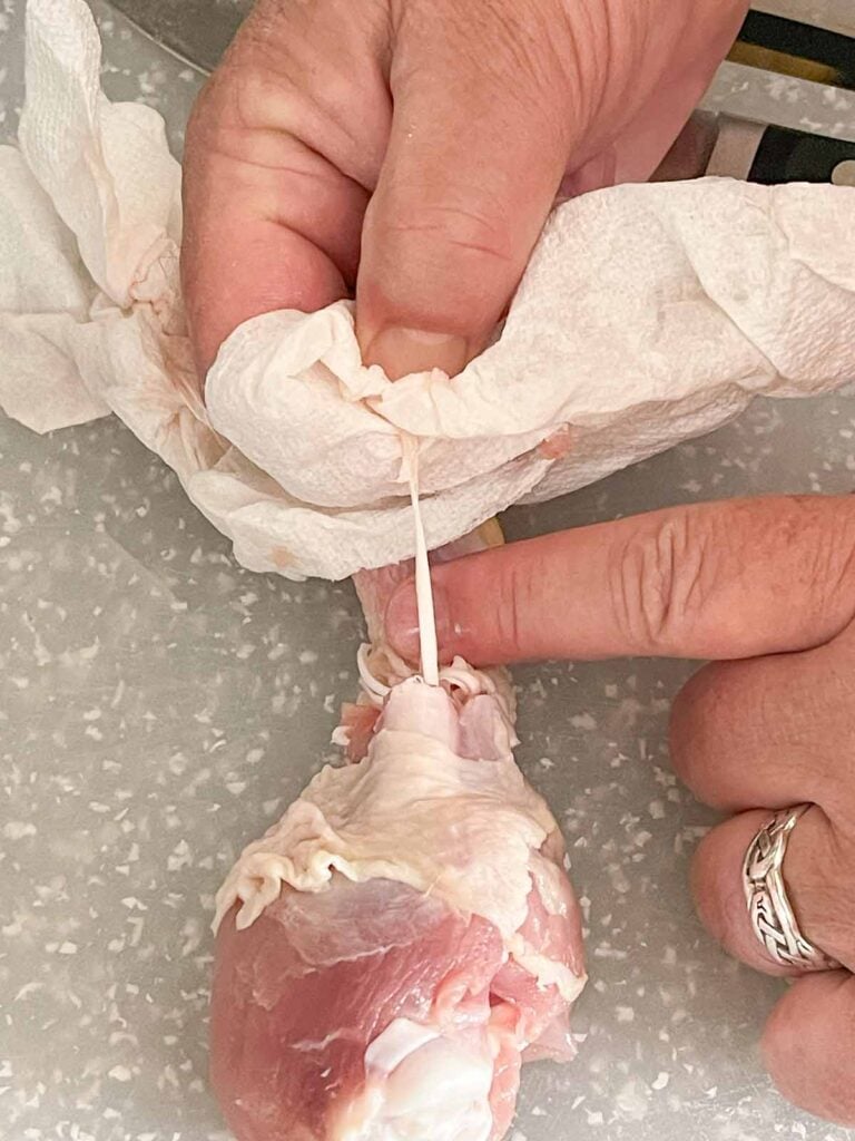 Using a paper towel for a better grip while pulling a tendon from a chicken drumstick.