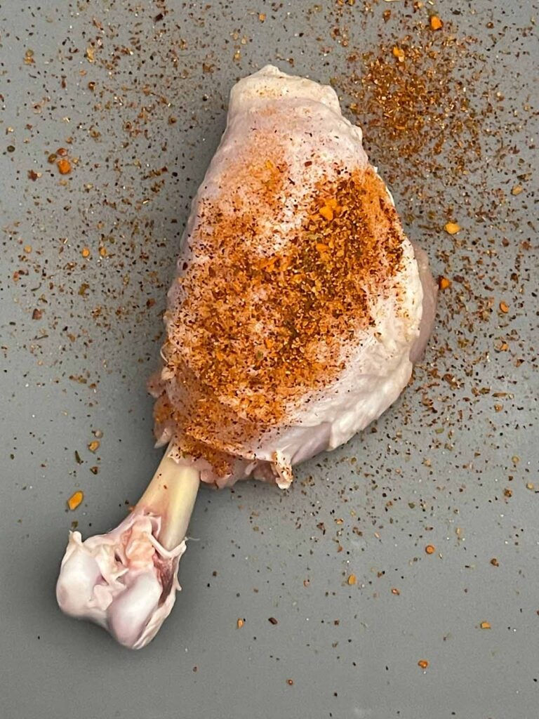 BBQ dry rub being sprinkled over a prepared chicken lollipop.