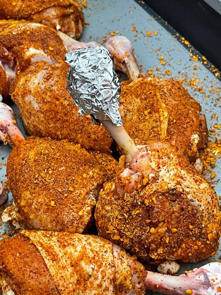 Seasoned chicken lollipops with aluminum foil wrapped around the exposed bone ends.