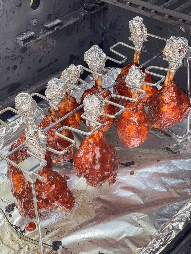 BBQ glazed chicken lollipops hanging on the smoker rack while the sauce sets.