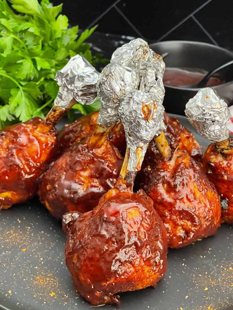 Smoked BBQ Chicken Lollipops with crispy skin and a sticky BBQ glaze served on a black plate.