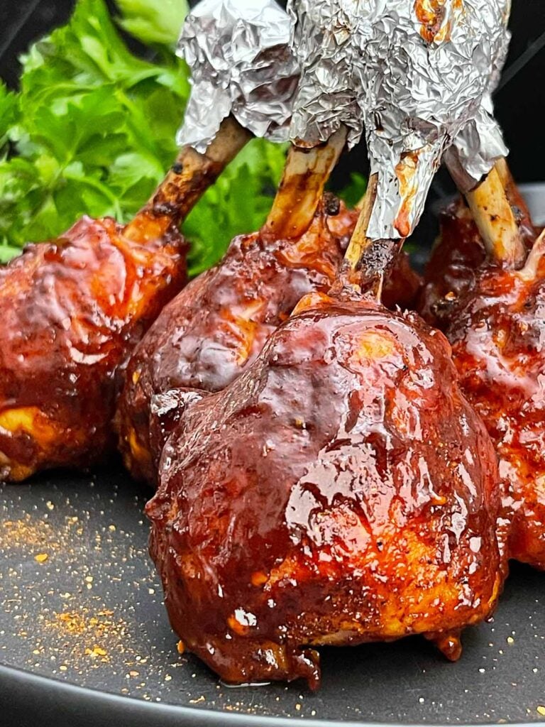 Smoked BBQ Chicken Lollipops with crispy skin and a sticky BBQ glaze served on a black plate.