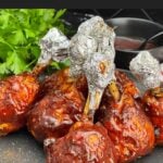Smoked BBQ Chicken Lollipops with crispy skin and a sticky BBQ glaze served on a black plate.