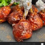 Smoked BBQ Chicken Lollipops with crispy skin and a sticky BBQ glaze served on a black plate.