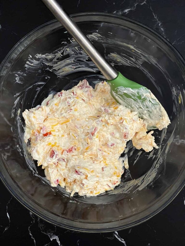 Cream cheese, sharp cheddar, mayonnaise, pimentos, garlic powder, onion powder, and black pepper mixed together in a glass bowl.