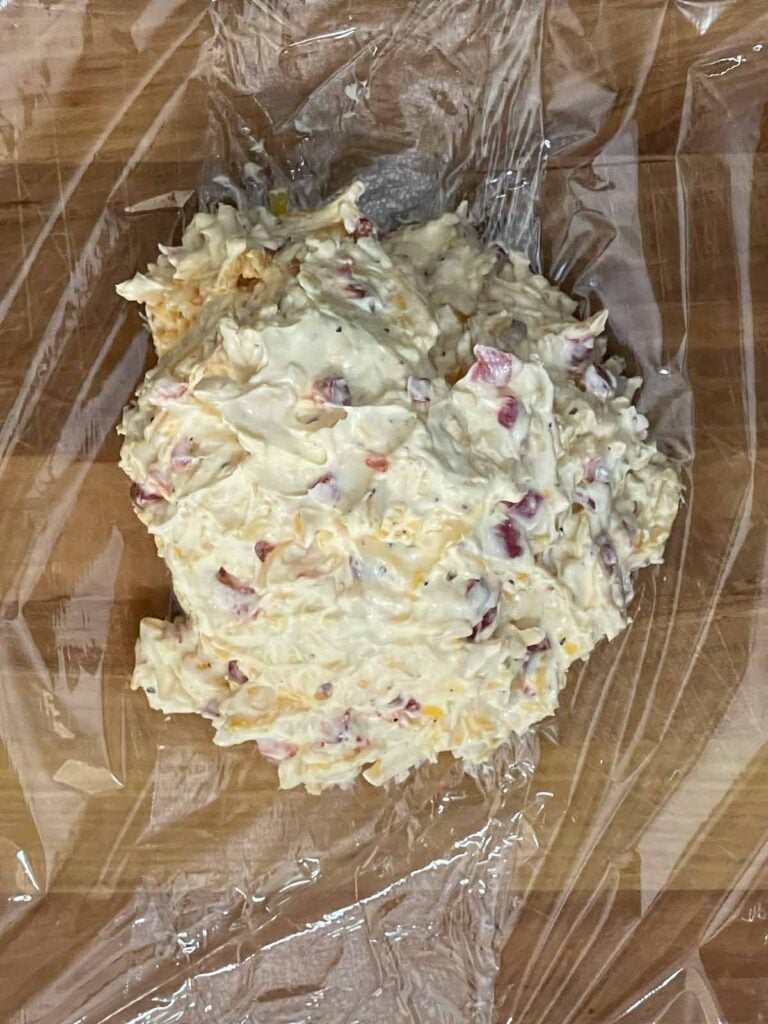 Pimento cheese mixture spooned onto plastic wrap for shaping.