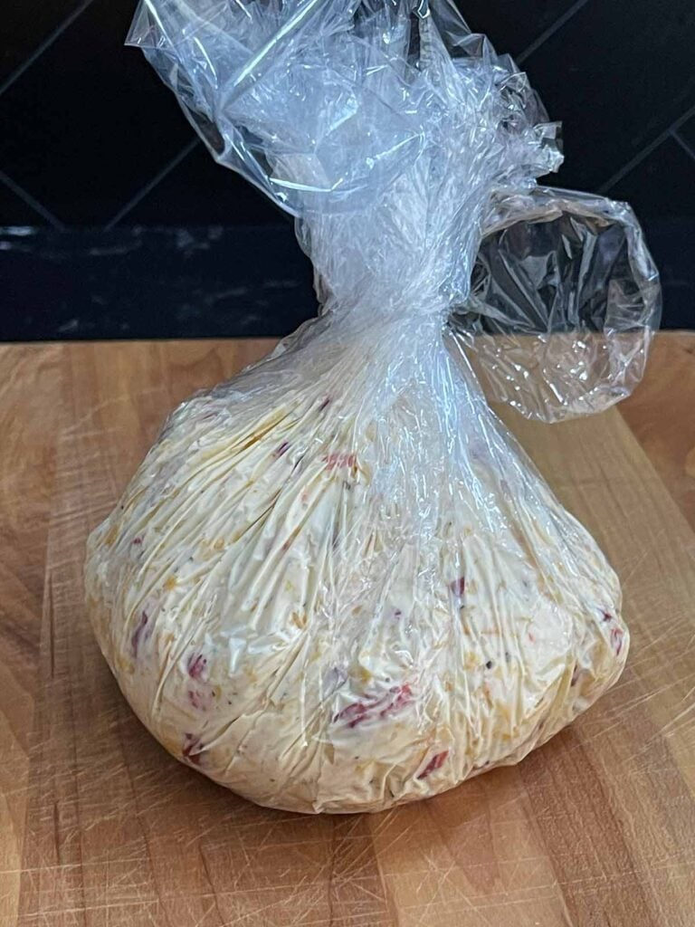 Pimento cheese mixture shaped into a ball and wrapped tightly in plastic wrap for chilling.
