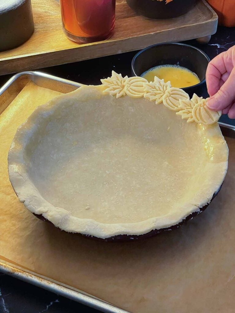 Placing pie dough cut out on the edge of the pie crust.