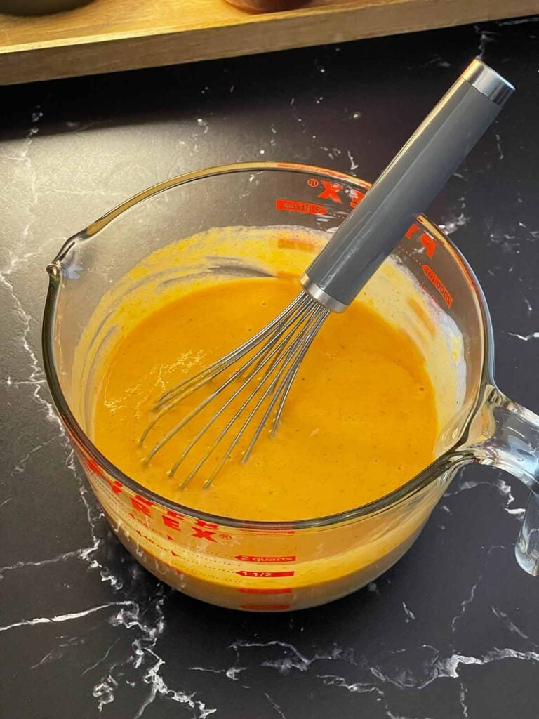 Pumpkin puree, eggs, eggnog, sugar, and spices whisked together in a mixing bowl.