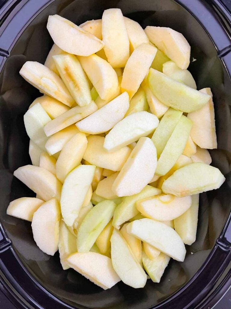 Peeled and sliced apples in the crock of a slow cooker.