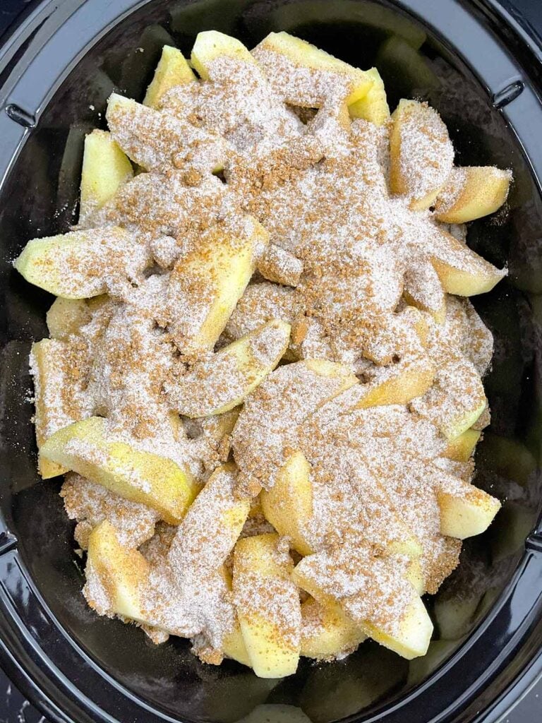 Peeled and sliced apples topped with brown sugar and warm spices in a slow cooker.